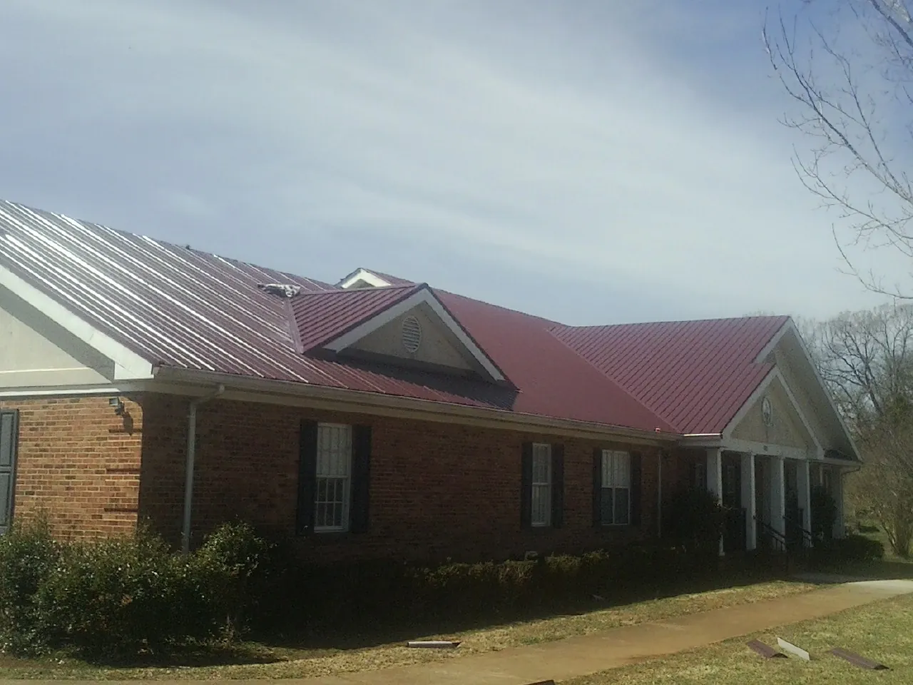 Red metal roof with gabled entries on a long brick building, from a Hail Damage Roof Repair job in Fleming Island