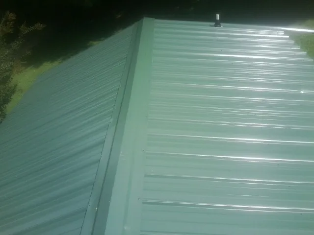 New green metal panels meeting at the ridge of a roof — Flat Roof Repair work by our crew in Fleming Island