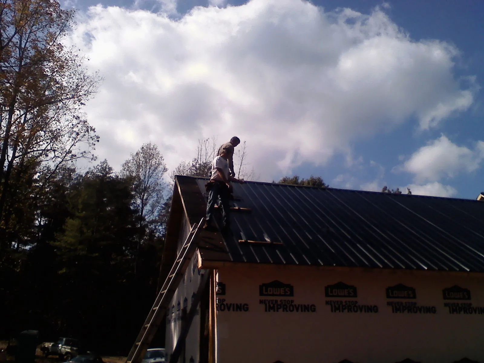 Roofer fastening dark metal panels high against a cloudy sky, from a Roof Inspection job in Fleming Island
