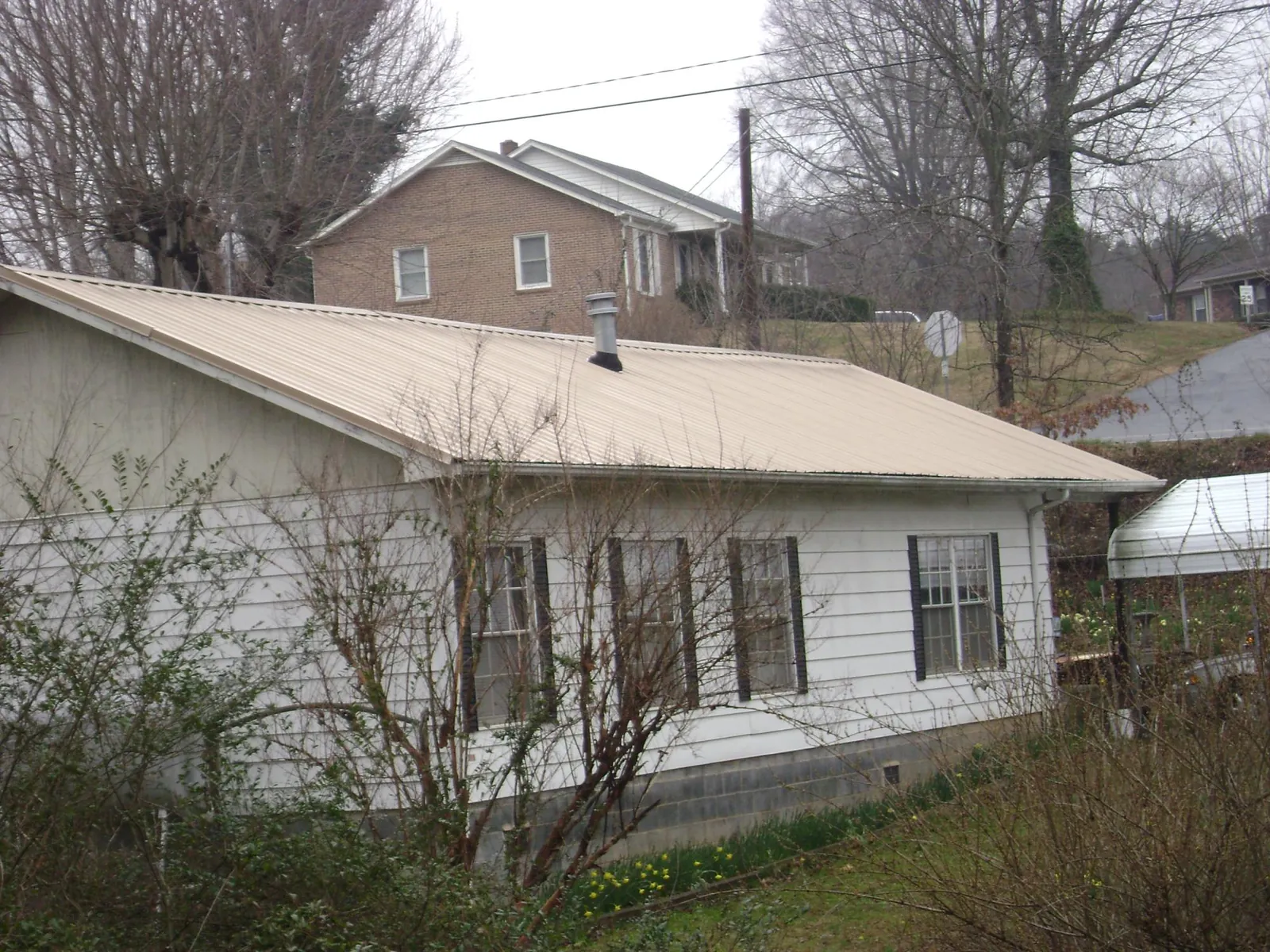 Tan metal roof on a white sided house set into a hillside — Commercial Roofing by Roofing Brothers in Fleming Island